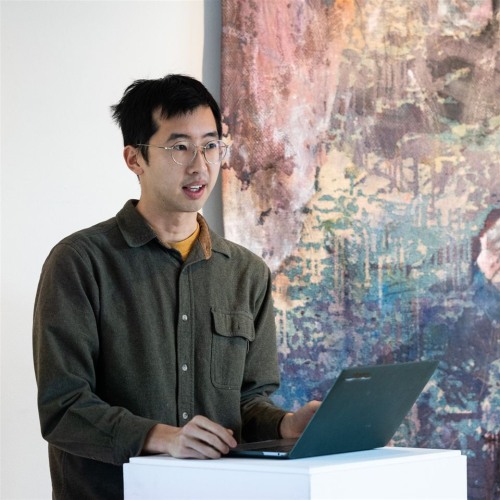 Justin Rui Han at a podium in front of a painting.